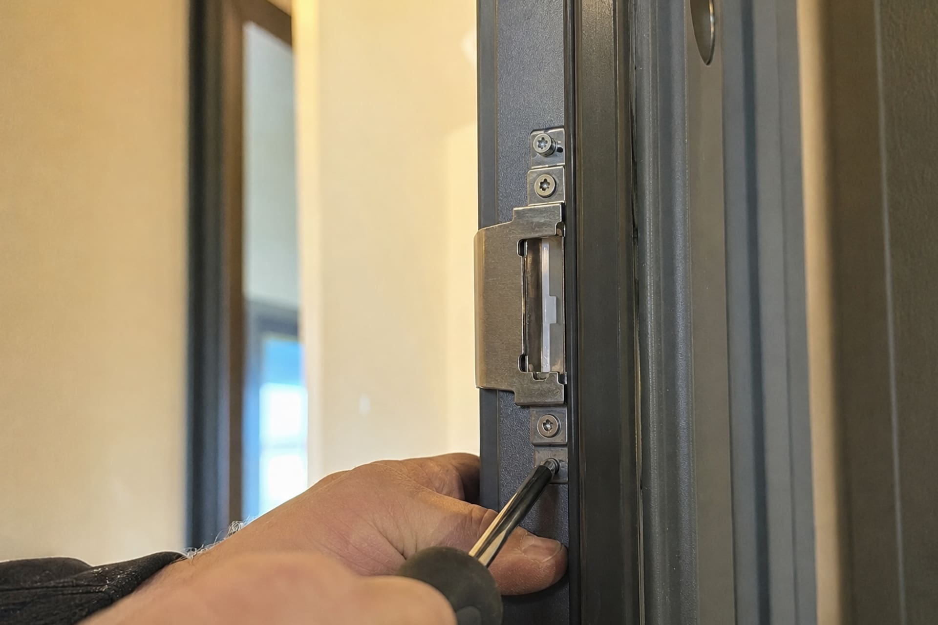 mains réglant une gâche de porte métallique